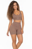 A woman modeling a matching two-piece shapewear set in taupe brown, featuring a sleeveless crop top and high-waisted shorts with lace trim, against a plain white background.